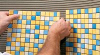 Процес приклеювання плитки мозаїки на стіну у ванній